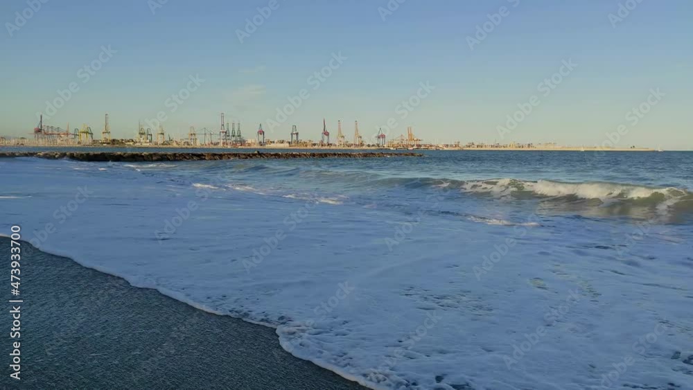 Sea waves run into deserted beach on sunset in summer. Seascape with several cranes in the port away Sea waves run into deserted beach on sunset in summer. Seascape with several cranes in the port away