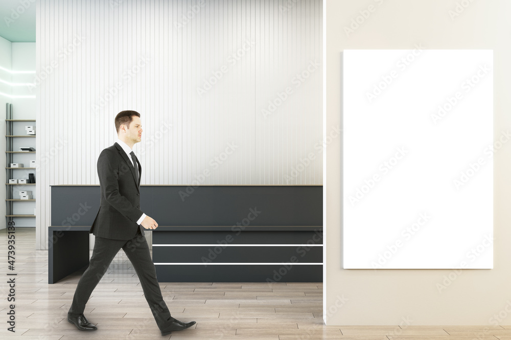 Businessman walking in modern concrete office interior with wooden flooring, black reception desk and white mock up poster on wall. Lobby concept. Businessman walking in modern concrete office interior with wooden flooring, black reception desk and white mock up poster on wall. Lobby concept.