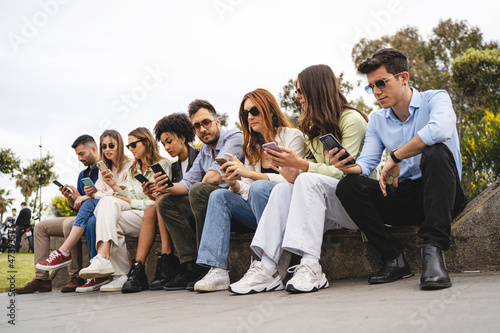 Group of young people sitting outdoors and using cellphone - Gen z young people phubbing