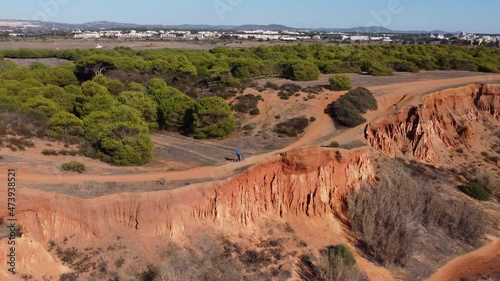 Aerial shot of praia da Rocha Baixinha in the Algarve following a cyclist who cycles over the dunes, sunny morning light.  Flying next to the cyclist in line of the dunes. Europe Portugal photo