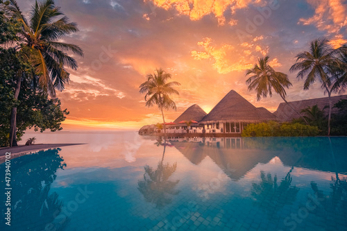 Sunset tourism landscape. Luxurious beach resort with swimming pool reflection beach chairs or loungers under umbrellas with palm trees, sunset sky. Summer travel and romantic vacation background