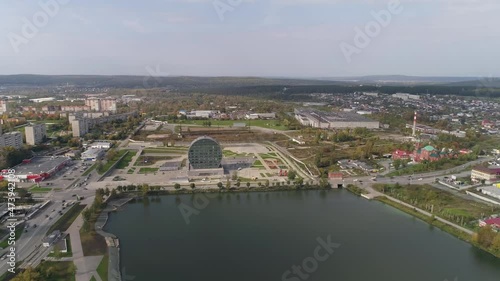 Aerial view of Modern building in the city in the form of a washer next to a pond. Cars drive on the roads. Summer sunny day. Near industrial zone. Russia, Pervouralsk city. High quality 4k footage. photo