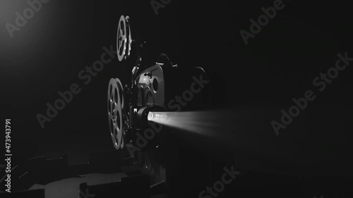 Monochrome shot of an old-fashioned antique 8mm film projector projecting a beam of light in a dark room. The camera flies around photo