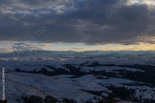 The setting sun illuminates the mountain range through the clouds