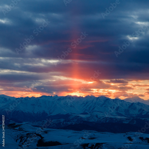 The setting sun illuminates the mountain range through the clouds