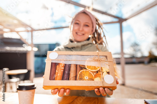 Defocused portrait of a young smiling woman with dreadlocks holding a craft box of dried fruits and pastille. Concept of natural sugar free sweets photo