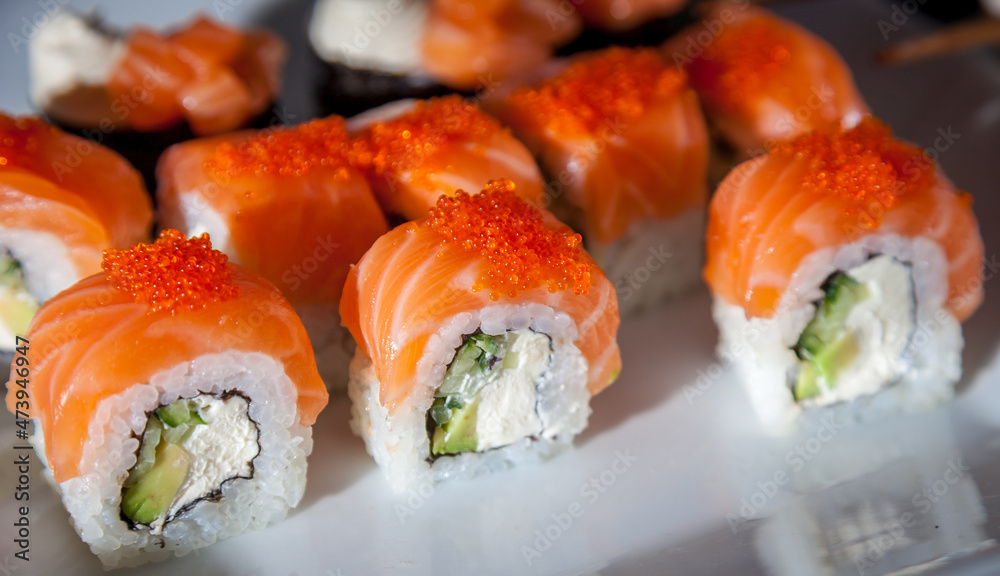Salmon sushi set. Sushi roll Philadelphia with red fish, salmon, red caviar. Roll with soft avocado and cream cheese under a layer of massago caviar. Classic sushi. Food background Salmon sushi set. Sushi roll Philadelphia with red fish, salmon, red caviar. Roll with soft avocado and cream cheese under a layer of massago caviar. Classic sushi. Food background