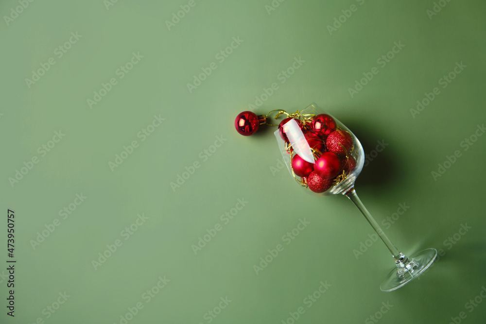 Fototapeta premium Wine glass filled with red christmas balls on green background.