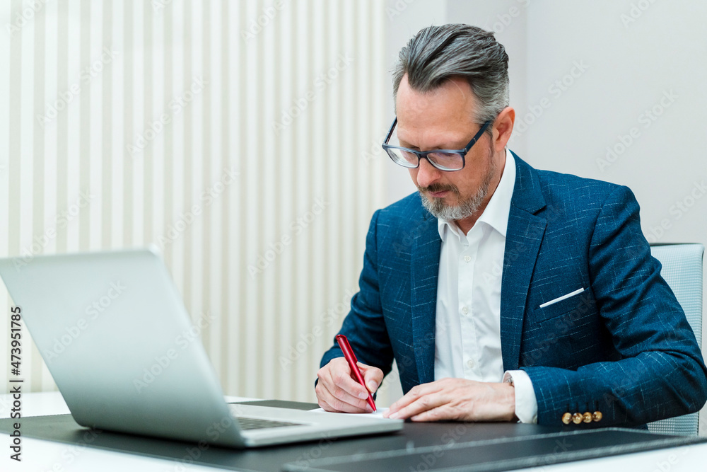Businessman with laptop writing in notepad while working at office Businessman with laptop writing in notepad while working at office