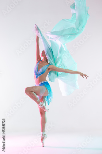 Classical Ballet Concepts. Young Professional Japanese Female Ballet Dancer Posing in Pale and Blue Dress With Flying Green Cloth In Hands Against White
