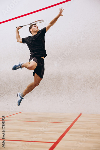 Full-length portrait of sportive boy training, playing squash in sport studio