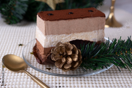 A piece of cake or chocolate pie or souffle decorated with pine cone branches of a Christmas tree on a light background. New year gifts, festive and festive concept.