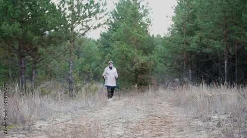 Outdoor Nordic walking. Senior woman walking in a pine forest . An active lifestyle in retirement, a hike in nature.
