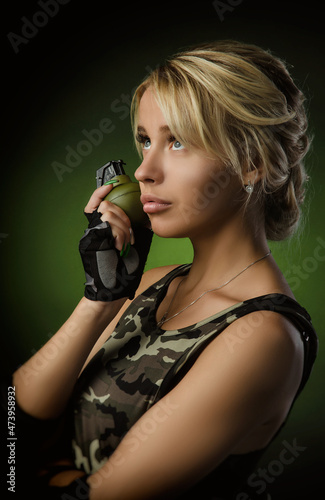 a girl in military airsoft clothes with a grenade in her hands on a dark background