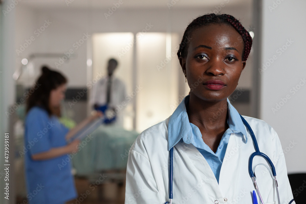 Portrait of african american practitioner doctor looking into camera working at disease diagnosis in hospital ward. Specialist therapist typing medical expertise on computer. Medicine services