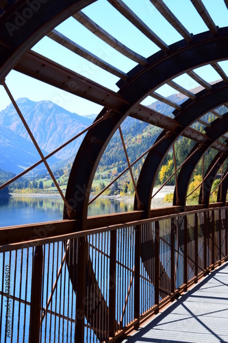 Talumrundung mit Zoggler Stausee und mit Holz verkleideter Brücke, Radweg und Wanderweg im Herbst, Blick vom See über das hintere Ultental mit den Alpen, Südtirol, Italien, Europa 