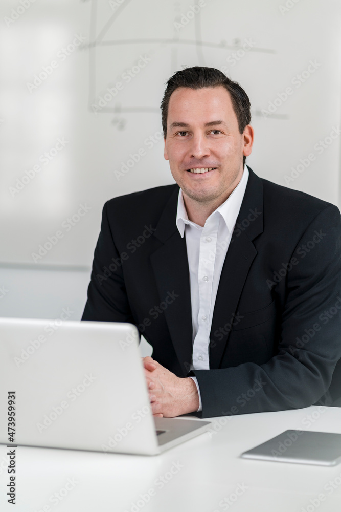 Smiling male professional sitting with laptop at desk in office Smiling male professional sitting with laptop at desk in office