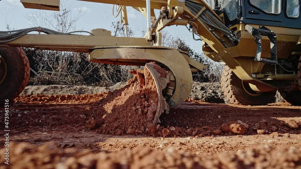 Tracking shot of yellow road grader smoothing gravel surface for highway road. Scraper leveling ground, working at construction. Earthmoving, excavations, digging on soils.