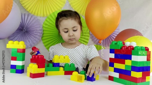 baby game. Little girl 4 years old plays with toy blocks on a colorful background of balls and decorations. games for early development.