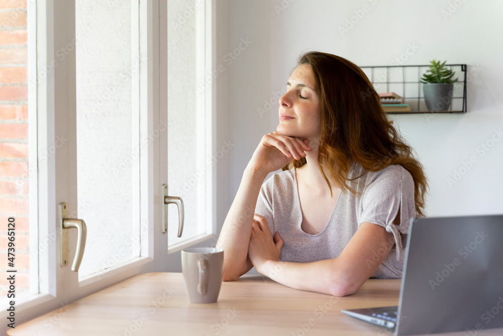 Woman with eyes closed sitting near window at home office Woman with eyes closed sitting near window at home office