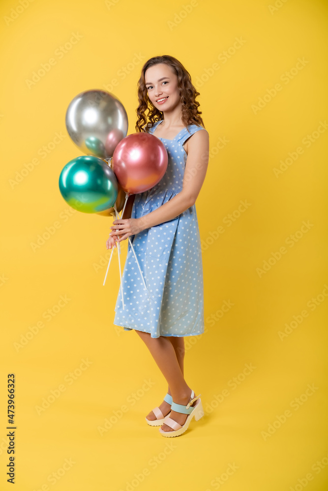 studio, beautiful woman. model on a yellow background in a blue dress holds balls, has fun in the camera. model pose. photo session, holiday. birthday studio, beautiful woman. model on a yellow background in a blue dress holds balls, has fun in the camera. model pose. photo session, holiday. birthday