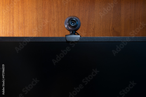External round black web camera on a black monitor. Webcam on a wooden background.