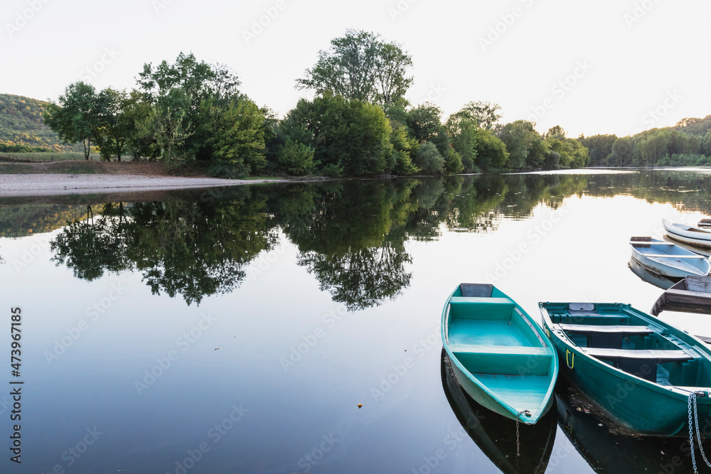 Trees reflecting in Dordogne River at dusk with moored boats in foreground Trees reflecting in Dordogne River at dusk with moored boats in foreground