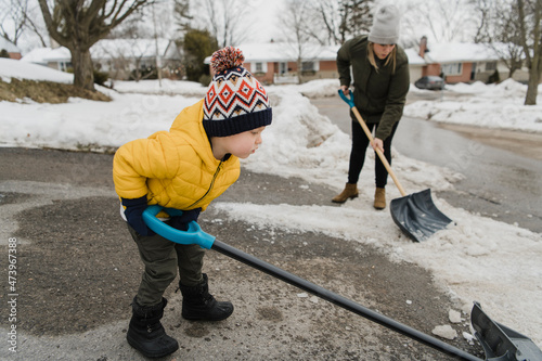 Son helping mother while shoveling snow on driveway