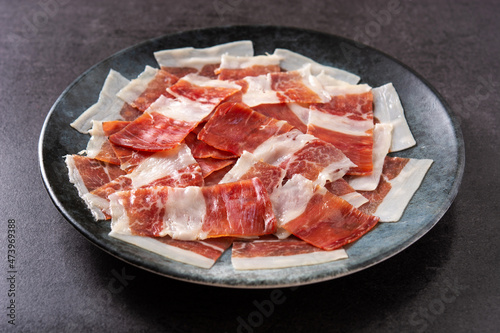 Spanish serrano ham slices on black plate on black background