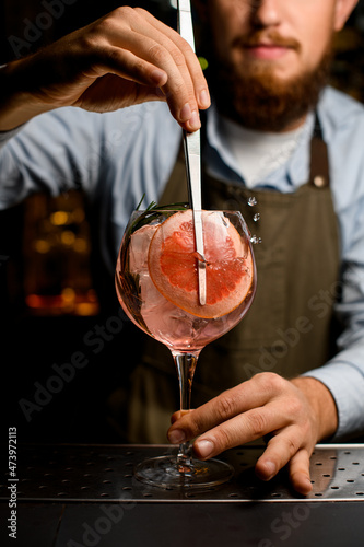 goblet glass with cold cocktail that the hand of barman decorating by fresh slice of grapefruit using tweezers