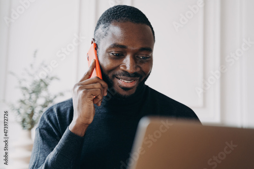 Fototapet Cheerful young man with African lineage commerce businessowner calling to suppli