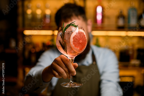male hand holds beautiful goblet glass with cold drink with slice of grapefruit and rosemary