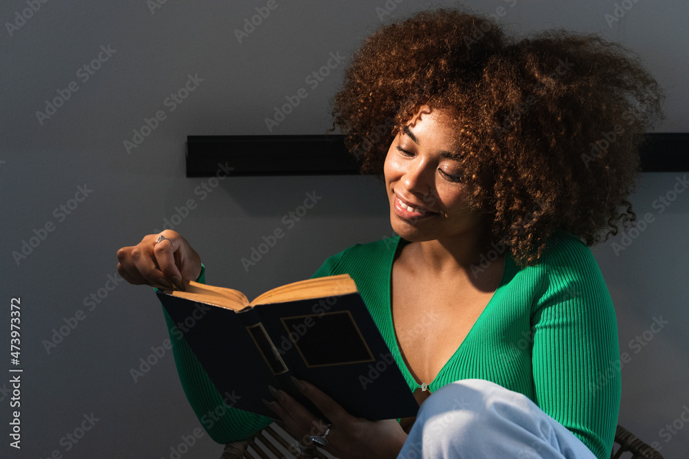 Young Afro woman reading book at illuminated home Young Afro woman reading book at illuminated home