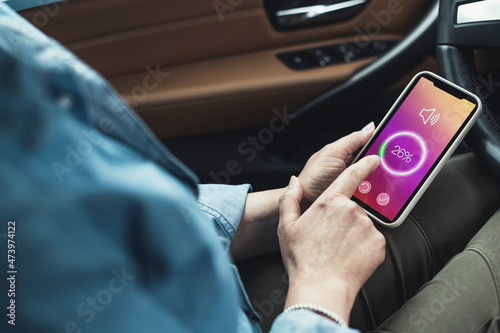 Woman adjusting volume through smart phone while sitting in car photo