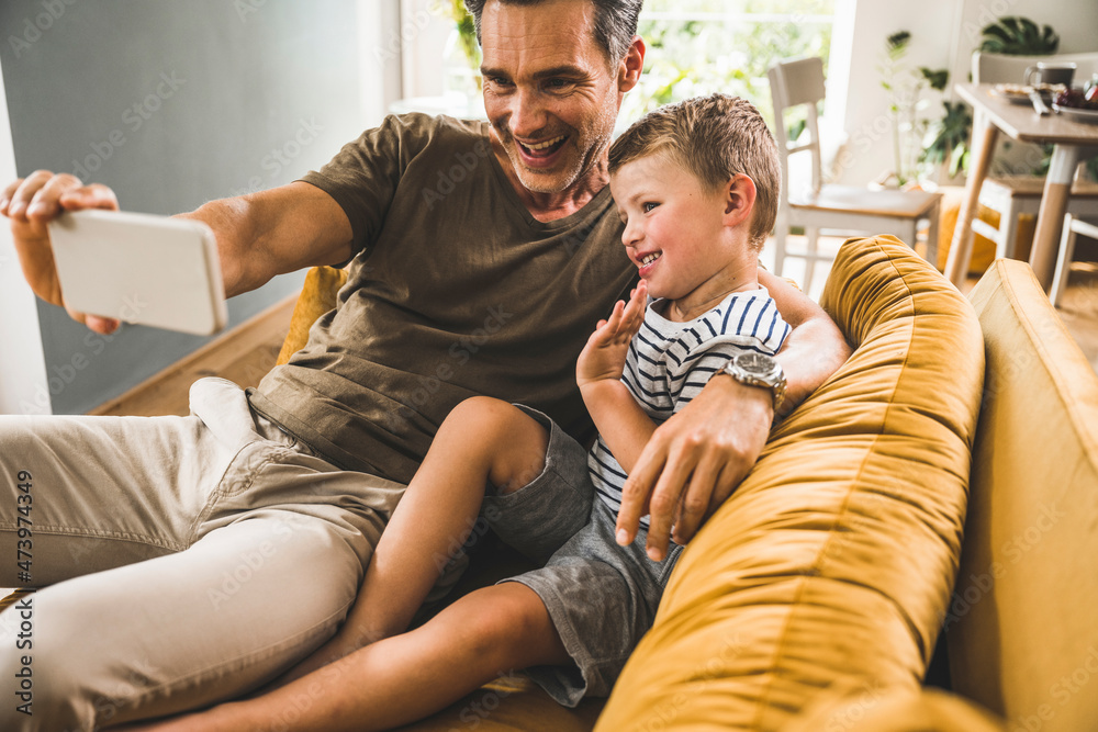 Father taking selfie with son through mobile phone at home Father taking selfie with son through mobile phone at home
