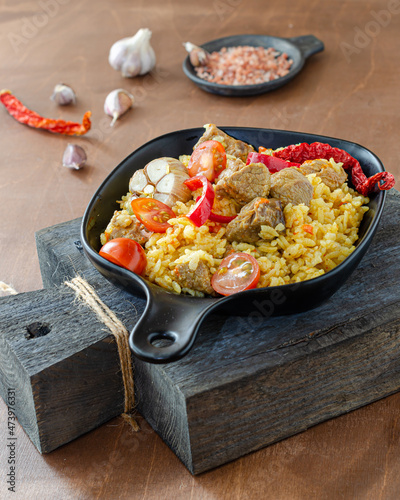 
Traditional oriental pilaf in a cauldron on a wooden table on a sunny day. Step-by-step recipe for real pilaf