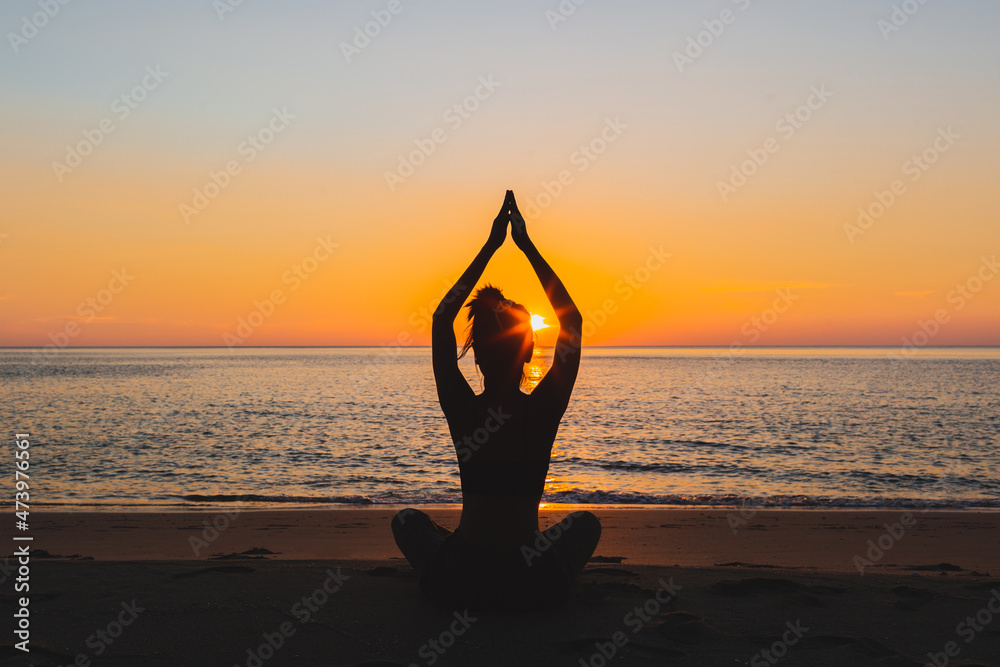 Silhouette of a woman meditating on the beach at sunset, outdoors.
  style silhouette