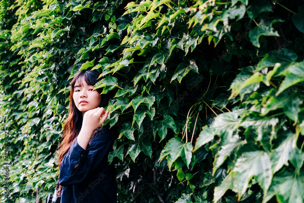 Young female photographer with camera standing in front of plants