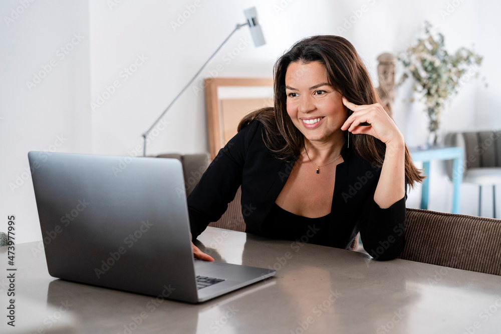 Mid adult businesswoman smiling with laptop at home
