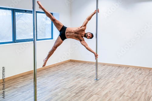 Shirtless male acrobat balancing on rod in dance studio