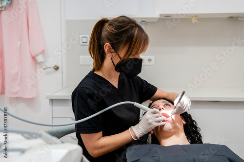 Female dentist wearing protective face mask doing dental suction of patient in clinic photo