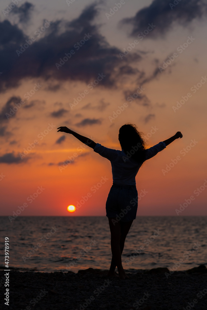 Happy young woman having fun with open hands at the sunset on sea.
