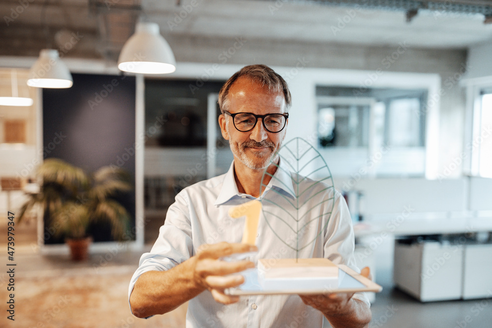 Businessman holding model while standing in office Businessman holding model while standing in office