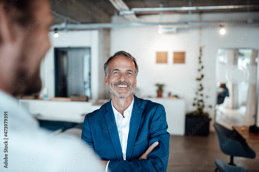 Businessman smiling while looking at colleague in office Businessman smiling while looking at colleague in office