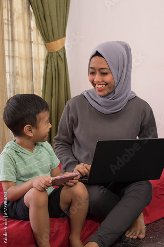 an Asian hijab mother is working from home using a laptop