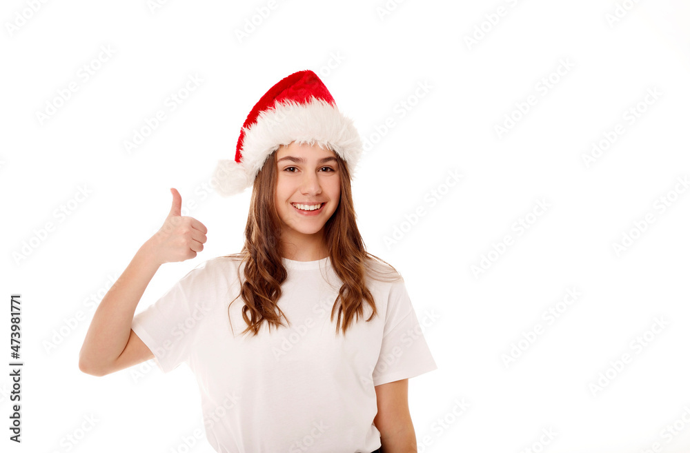Young happy teenager girl in Santa Claus red hat standing over white background smiling with happy face showing hand ok sign. Christmas and New Year lifestyle concept Young happy teenager girl in Santa Claus red hat standing over white background smiling with happy face showing hand ok sign. Christmas and New Year lifestyle concept