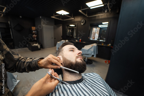 Hairdresser doing haircut of beard using comb and scissors