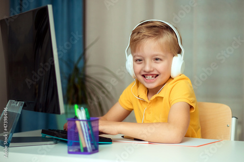 Happy child boy in headphones during online learning at home doing homework