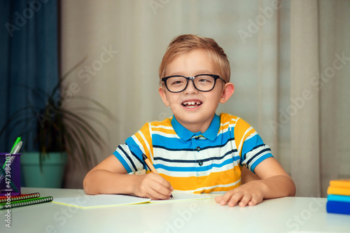 School child with glasses is doing homework sitting at the table at home.