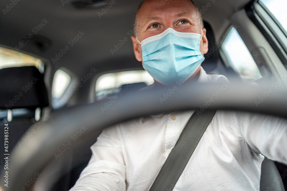 A man in a protective mask driving a car, steering wheel in the foreground